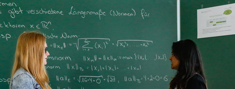 Two students standing in front of a blackboard